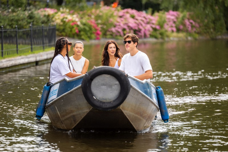 Vier vrienden varen samen in een kleine boot over een rustige gracht, omringd door groen en bloeiende struiken