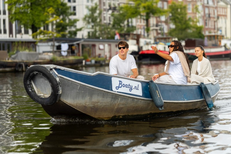 Drie vrienden varen met een kleine huurboot door een Amsterdamse gracht terwijl ze genieten van het uitzicht op de stad.