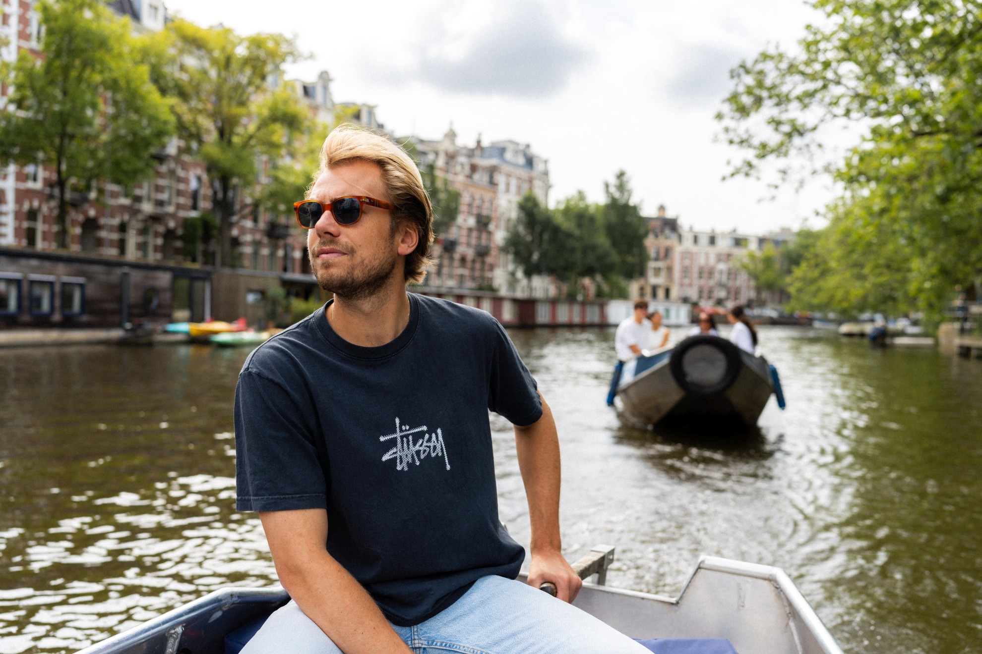 Man bestuurt een sloep op de Amsterdamse grachten en een ander bootje volgt hem op het water.